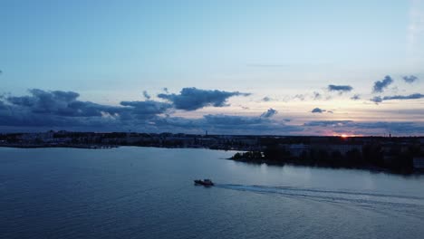 fishing vessel motors on sea as sun sets over deep blue helsinki, fin