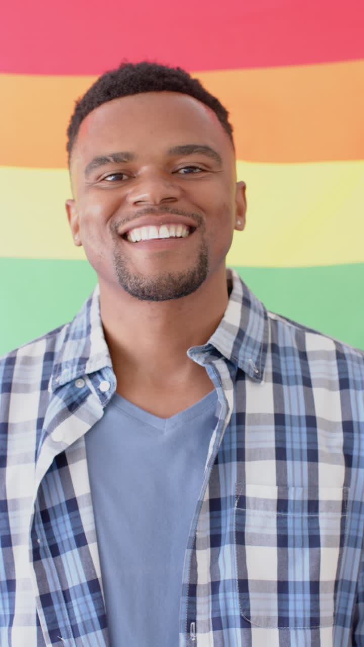 Vertical video of portrait of happy african american man holding lgbt rainbow flag, slow motion
