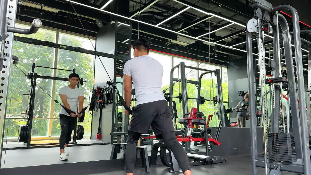 A trainer guides a workout on a pulley machine in a modern gym with natural lighting