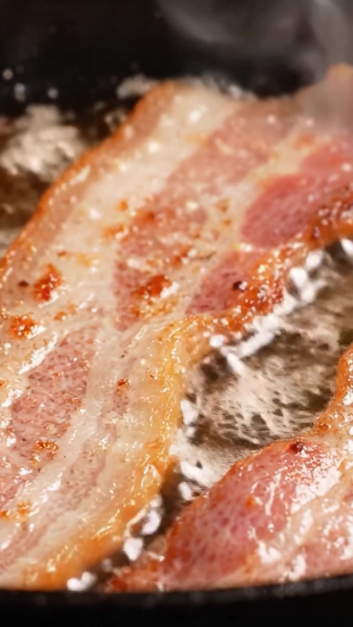 Lækkert sprød bacon steger på en varm pande: Et nærbillede af sydende svinekød, perfekt smeltet fedt og en mundvandsløbende tekstur for kulinariske entusiaster.