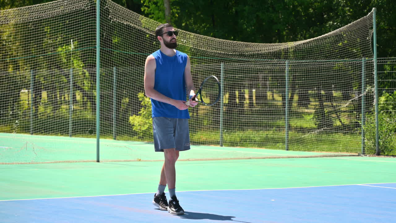 Man in blue shirt playing tennis on a blue and green court on a sunny day