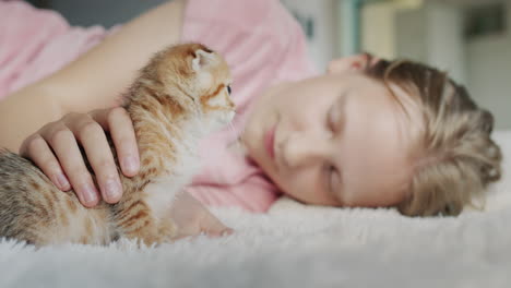 the girl lies on the floor in the house, next to her is her pet - a red kitten.