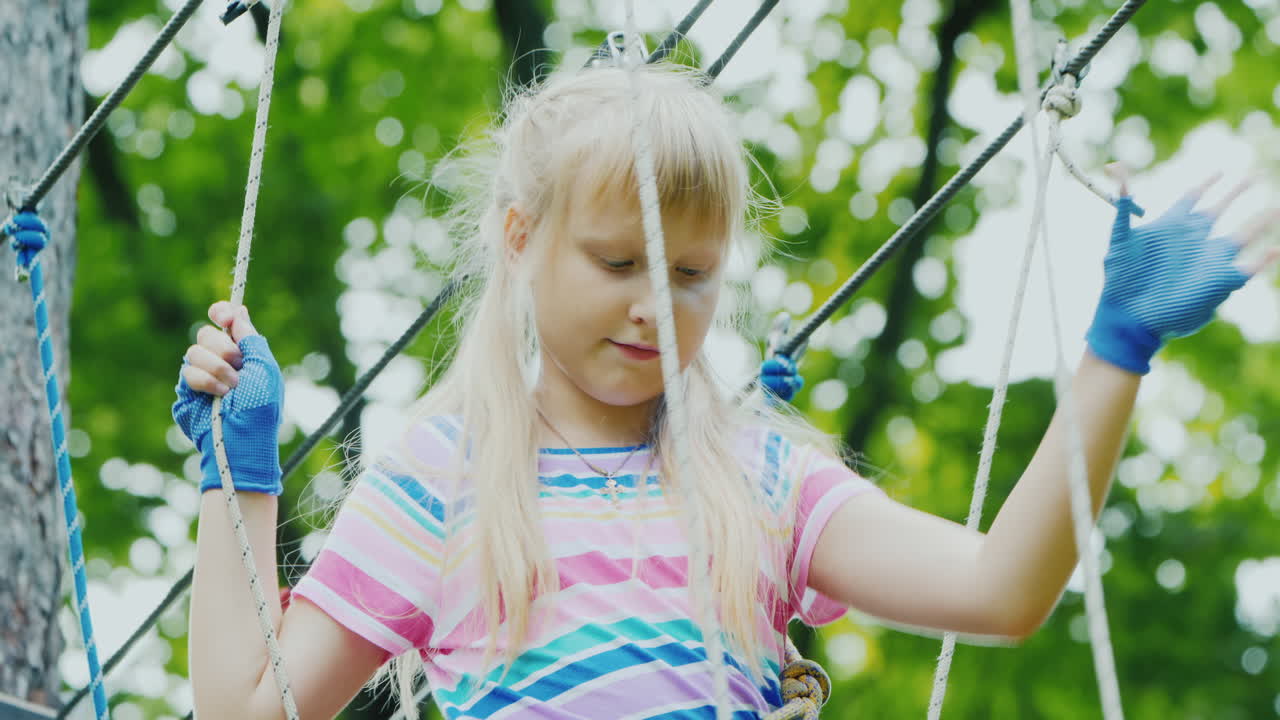 나무 사이의 밧줄을 따라 움직이는 용감한 소녀의 뒷모습은 안전 밧줄을 사용합니다