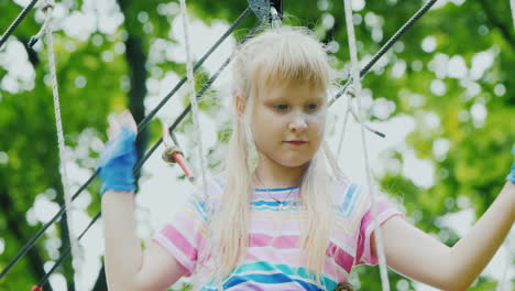 rear view of a brave girl moves along the ropes between the trees uses a safety rope