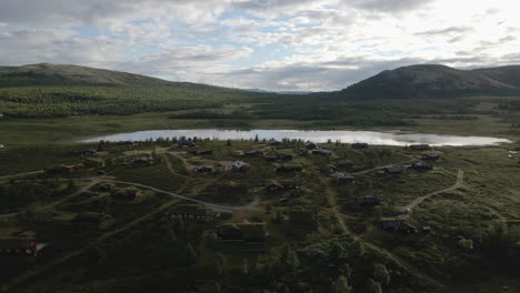 aerial shot of houses in the green valley with lake and mountain in the background venabygd, norway