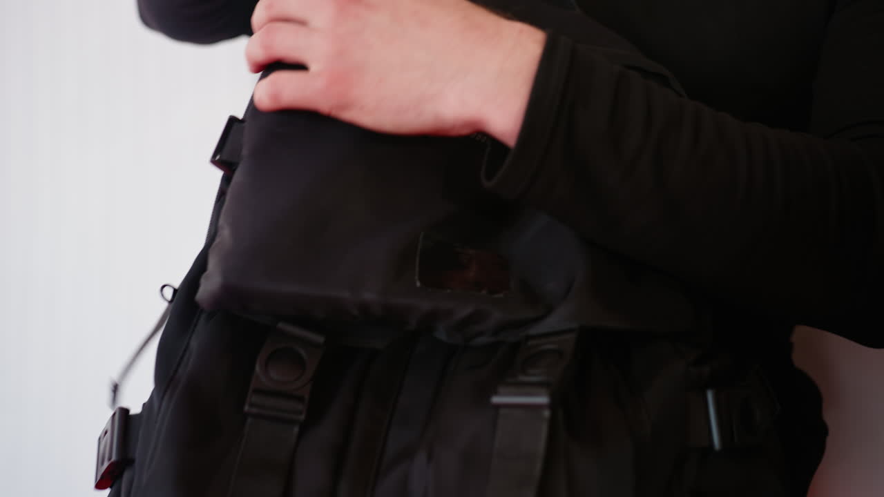 Policeman in black uniform sitting indoors holding bags preparing for training session, symbolizing readiness, discipline, teamwork, strength, focus, professional