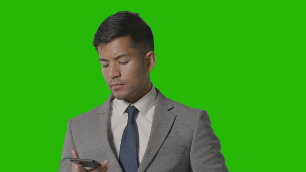 녹색 화면에 대해 휴대 전화로 전화를 받는 소송에서 심각한 사업가의 스튜디오 샷