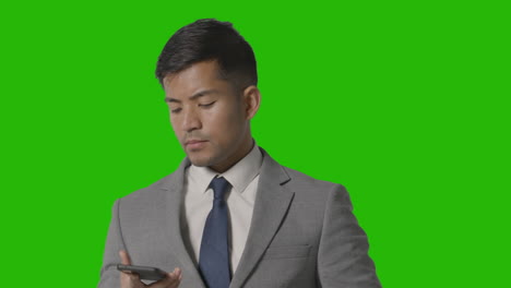 studio shot of serious businessman in suit taking call on mobile phone against green screen