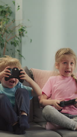 happy siblings control gaming consoles to compete playing exciting video game. little boy and girl have fun at home sitting on couch in living room