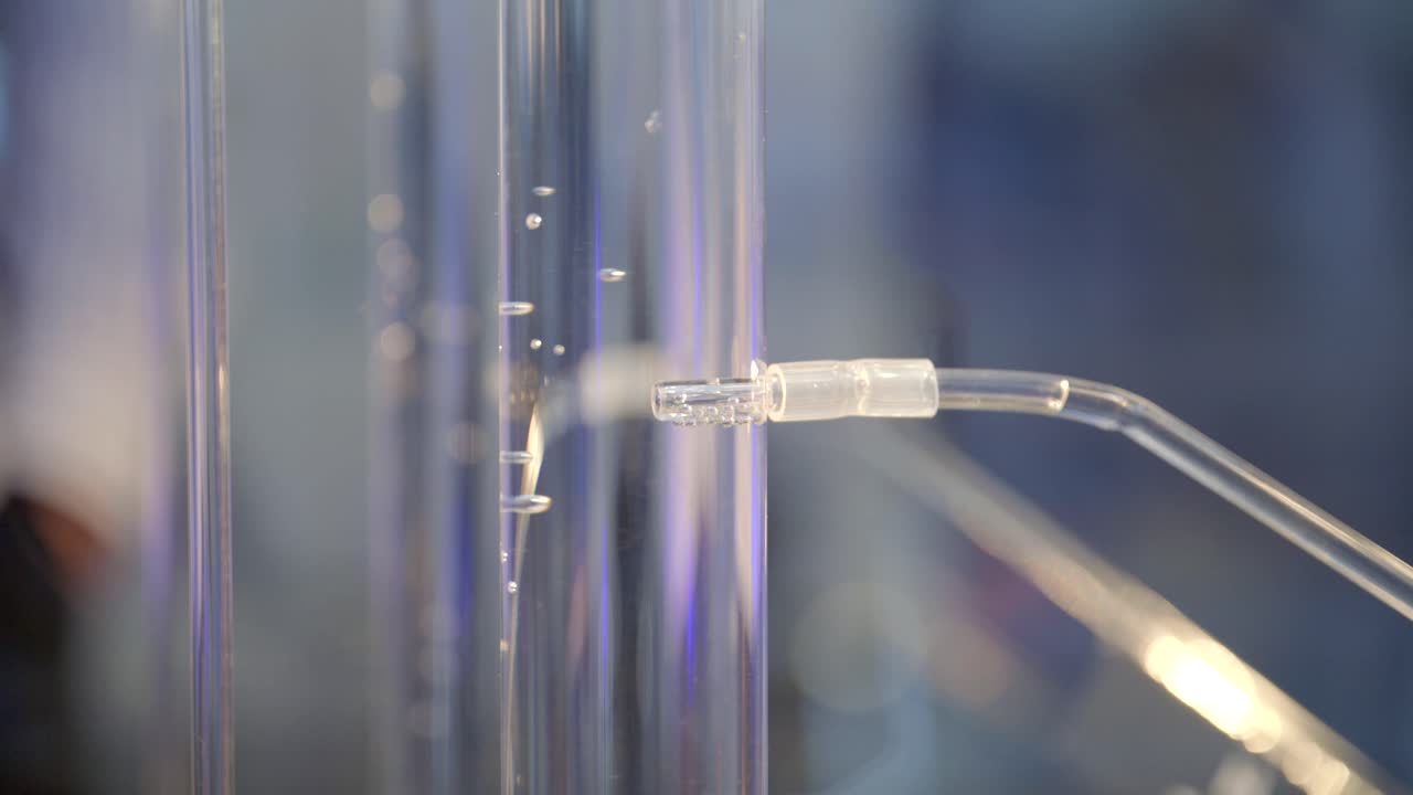 Bubbles of hydrogen gas flow from an electrolyzer into a glass cylinder filled with water, slow motion