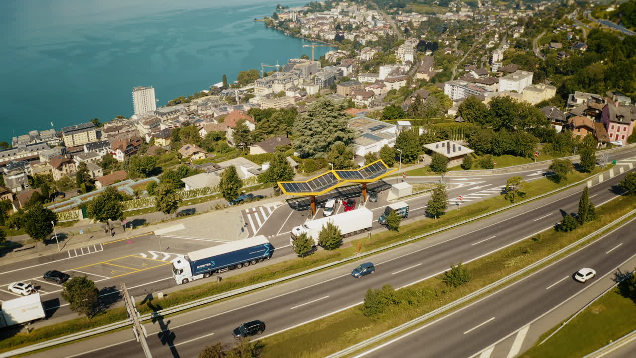 Aerial view of highway with cars and trucks passing a toll booth near a town by a lake