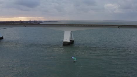 Órbita-Aérea-Sobre-Un-Hombre-Montado-En-Un-Ala-Aerodinámica-Frustrando-Cerca-Del-Puente-Más-Largo-De-Zeelandbrug-En-Holanda