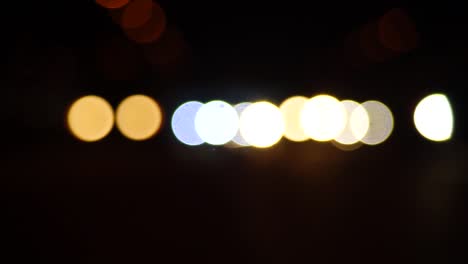 Steady-stream-of-car-headlights-out-of-focus-traveling-toward-the-viewer,-bokeh-balls,-blurred-lights,-dark-tunnel