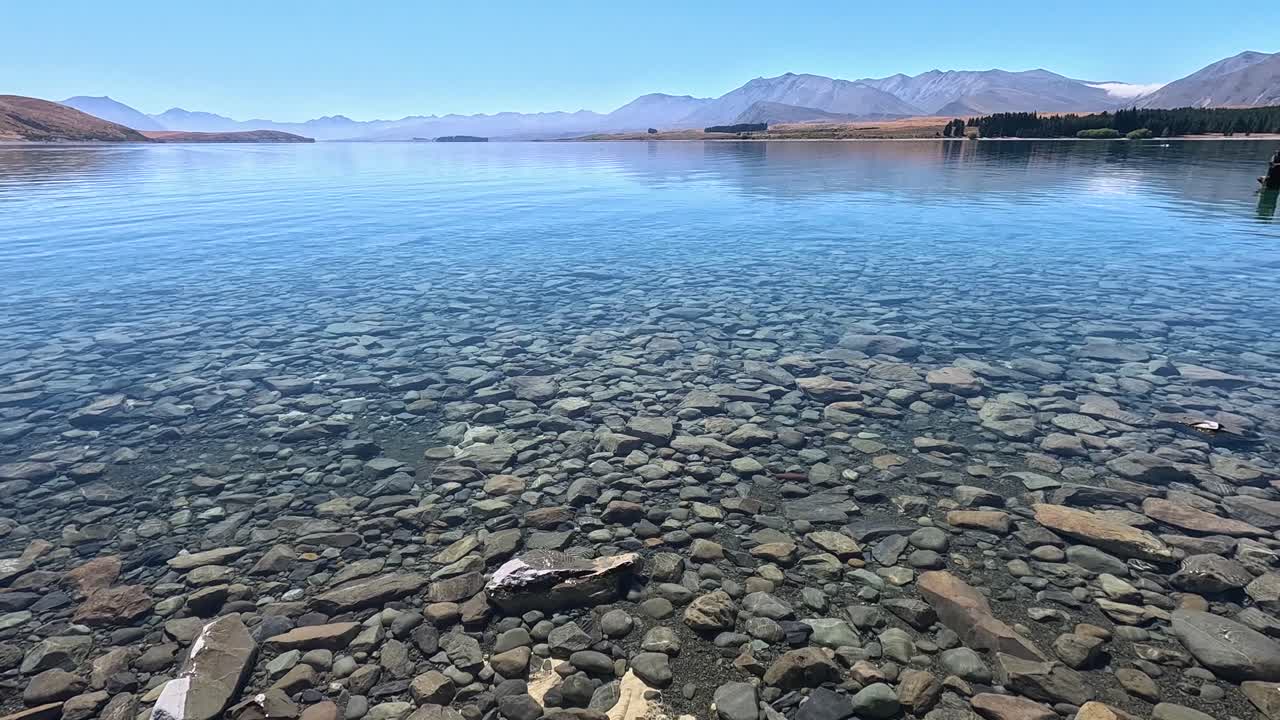 POV from a girl walking up and revealing Lake Tekapo in New Zealands south Island. You can see the rocks and stones initially and then it pans up to reveal the beautiful lake and mountains