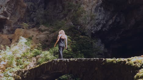 Mujer-Caminando-Sobre-Un-Puente-Natural,-Paisaje-De-Cuevas-Rocosas---Plano-General