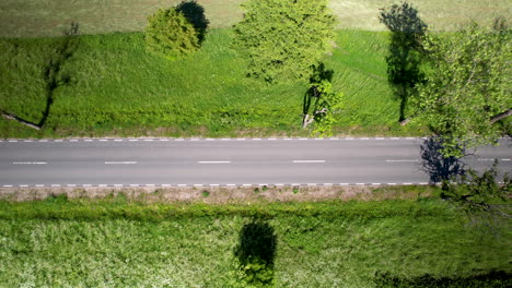 Drone-Aéreo-Volando-Sobre-Exuberantes-Campos-Verdes-Al-Lado-De-La-Carretera