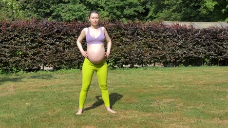 pregnant caucasian woman bending over to stretch in the garden