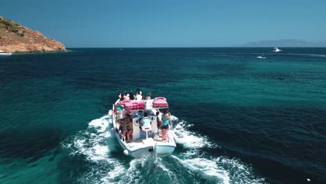Drone-shot-following-a-flowing-cruising-boat-with-tourists-at-sea-exploring-the-coast-during-their-vacation-on-a-sunny-clear-day