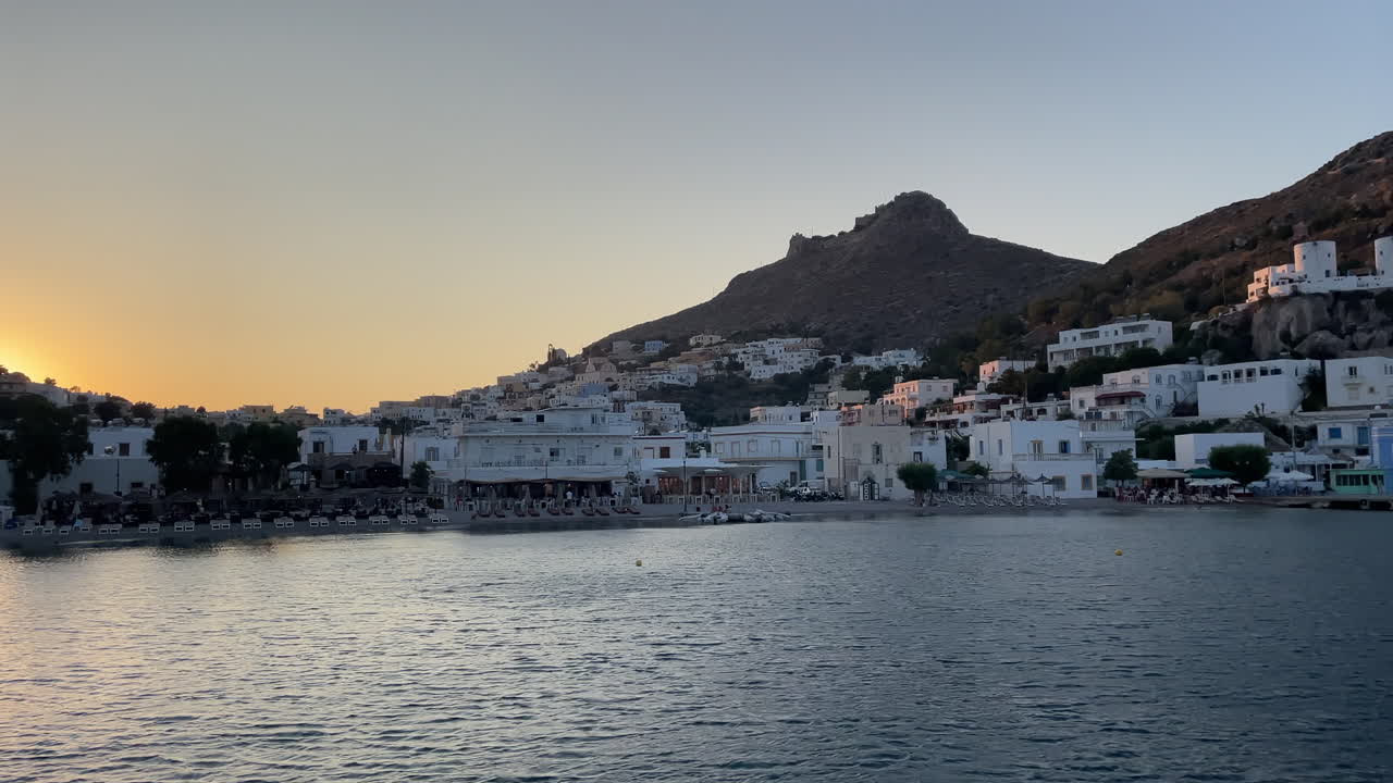 Greece,Leros Island, Panteli Town and beach footage from the sea during sunset, castle and windmills at the hill when sun is changing colors slightly during sunset.