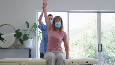 Female-health-worker-stretching-arm-of-senior-woman-at-home