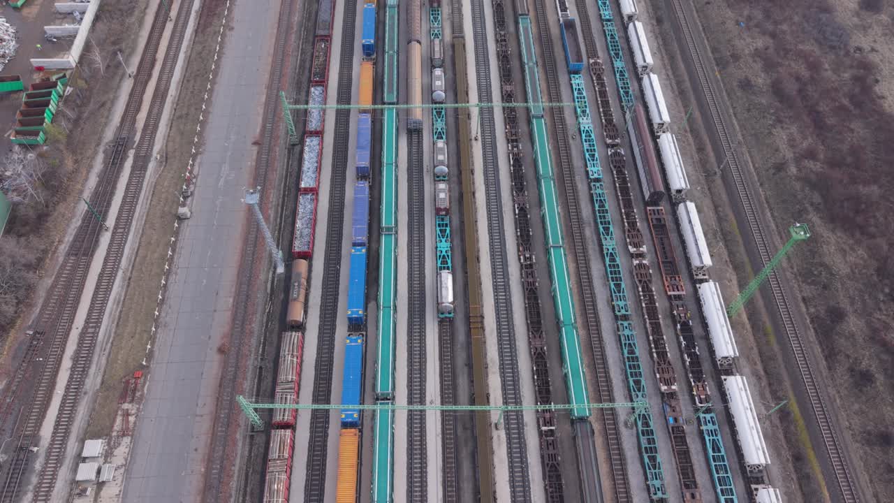 Aerial top view of a large railway yard with multiple freight trains and cargo wagons standing on parallel tracks