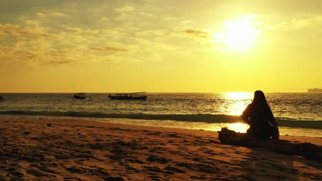 Silhouette-of-young-woman-watching-peaceful-sunset-with-yellow-sky-reflecting-on-sea-surface,-boats-sailing,-Antigua