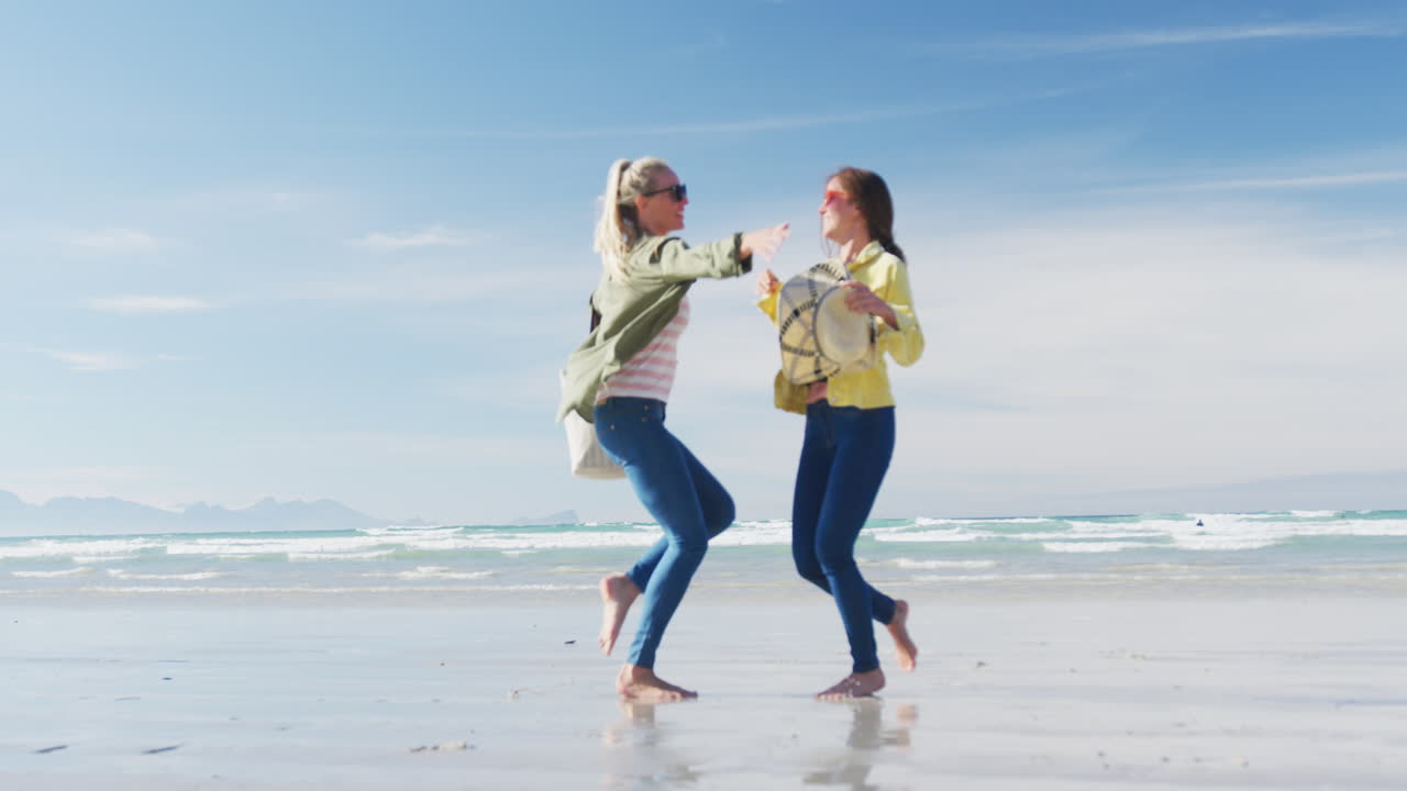 dos felices amigas caucásicas divirtiéndose, caminando por la playa