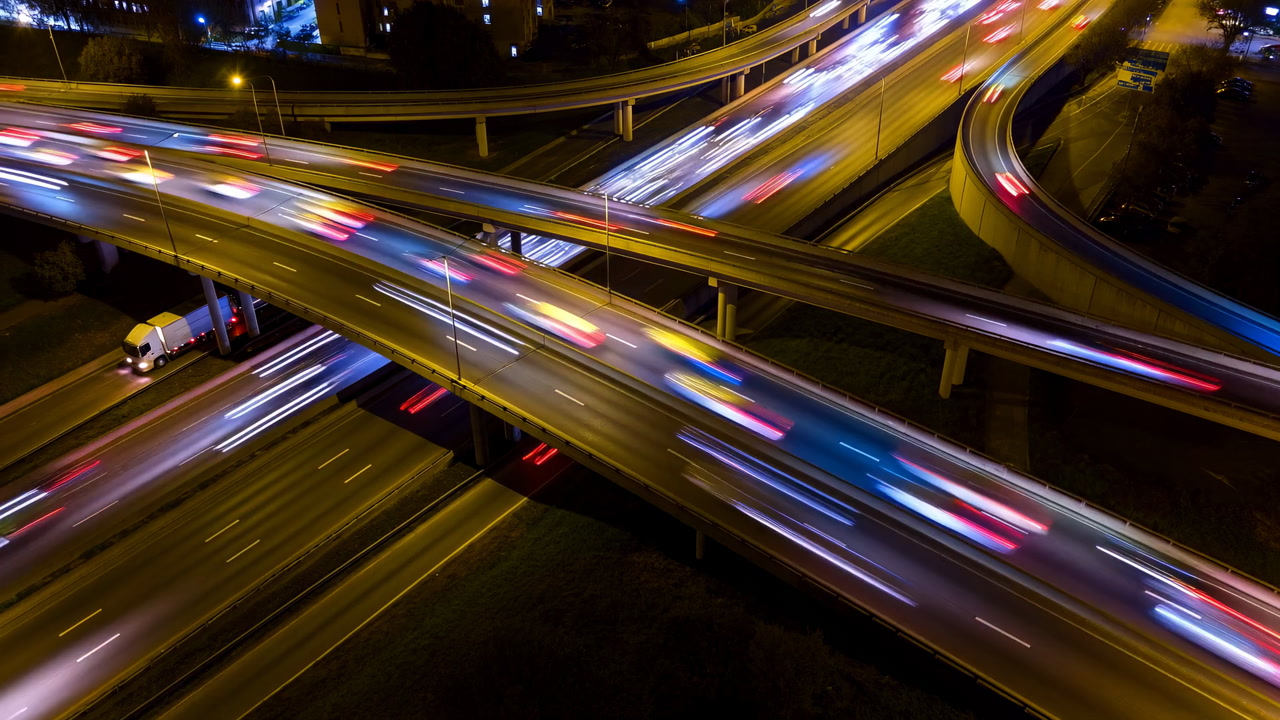 Aerial Night View Of Highway Interchange, Dynamic Light Trails Across Multilayer Overpasses, Flowing Traffic