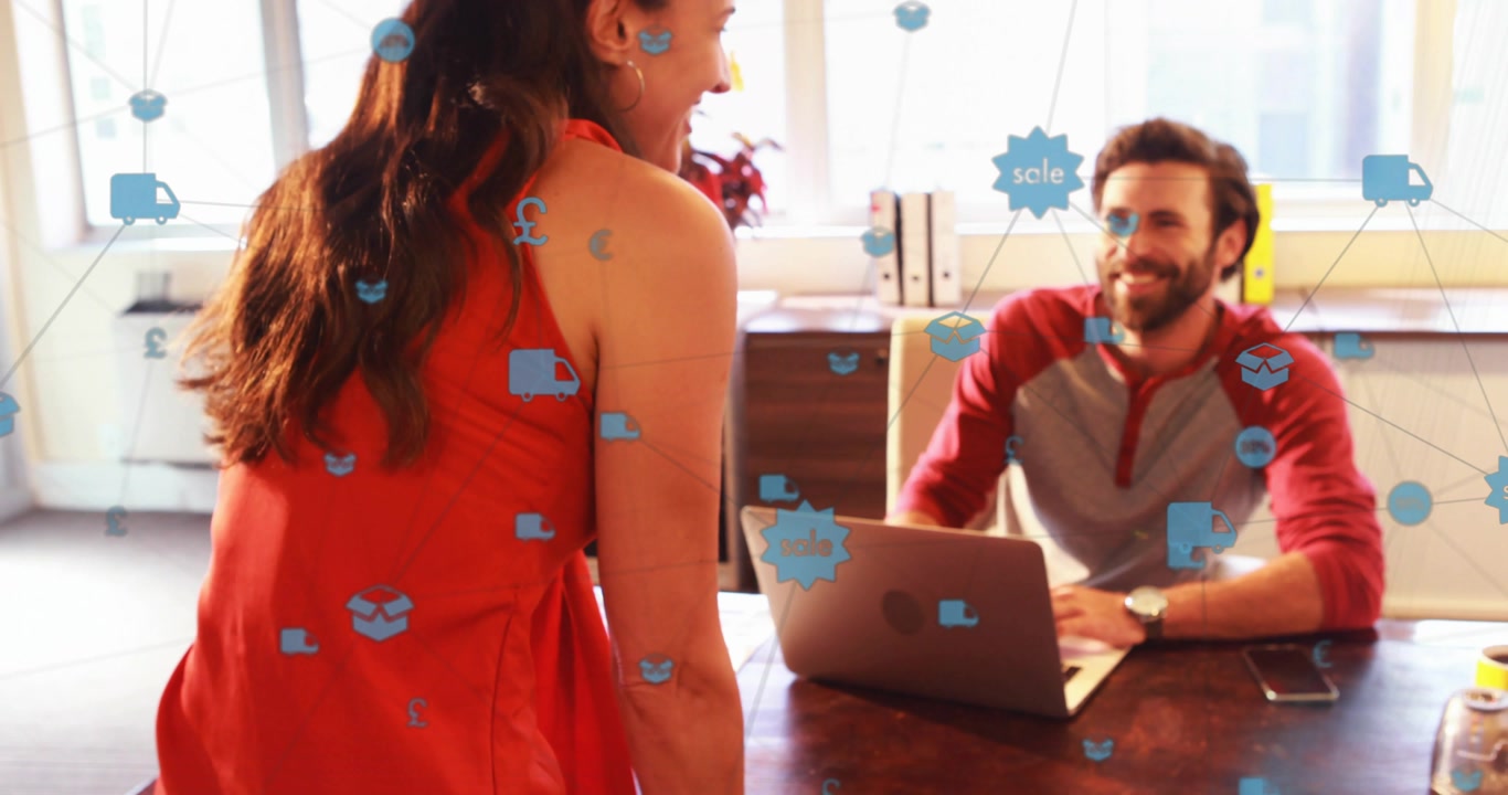 Diverse coworkers leaning at desk in office woman in red dress sharing laptop prints with icons