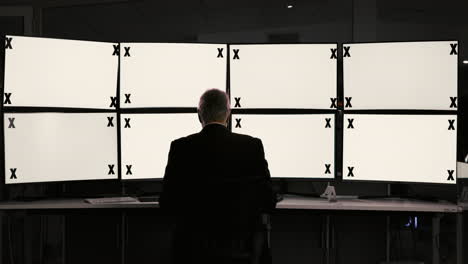 businessman monitoring multiple screens in a dark office