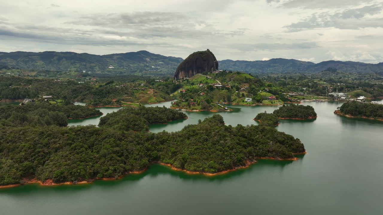 Panoramic drone shot of the lake and the El Pe&ntilde;&oacute;n monolith, in cloudy Guatape, Colombia