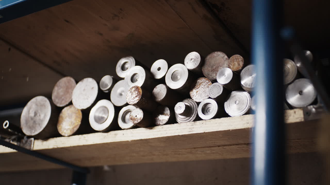 Vedute dettagliate di un'officina di lavorazione metalli industriale con scaffalature di stoccaggio di tubi d'acciaio grezzi, barre e utensili per la lavorazione.