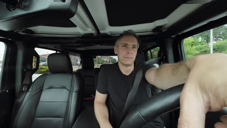 an adult man driving a car waits at an intersection