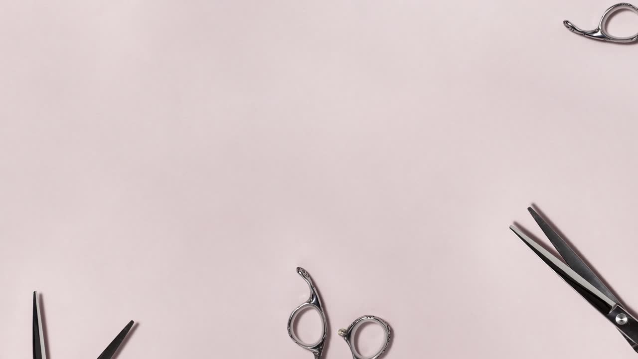 Flat lay of professional silver hair cutting shears set frame moves to the left on pink background. Hairdresser salon equipment and haircut work tools concept during quarantine with copy space