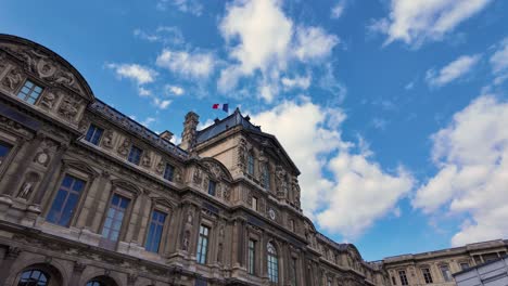 Louvre museum building Paris France French flag over blue sky with clouds