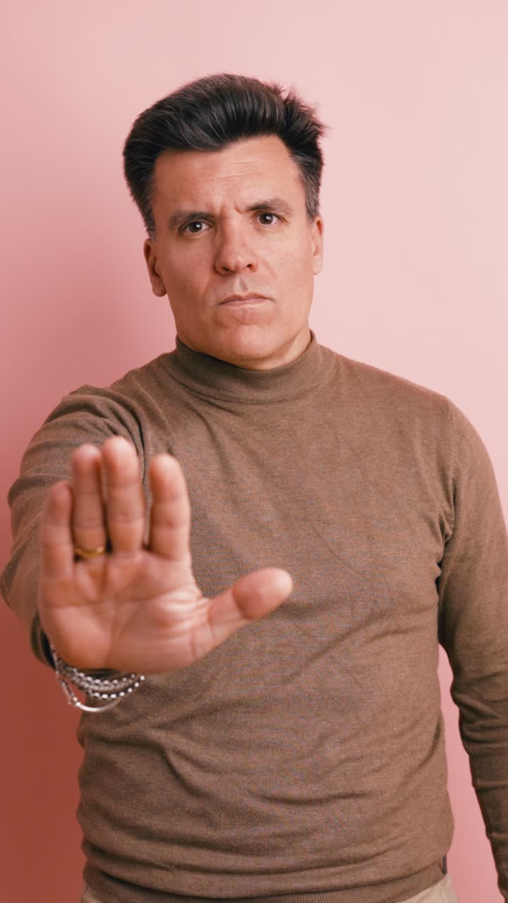 Serious Man Gesturing Stop with Hand on Pink Background