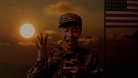 close up of asian man soldier looking at smartphone, smiling, and saying wow while standing with flag of the united states, sunset time