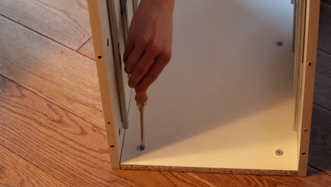 young boy's hand screws shelf parts together at home, on the floor