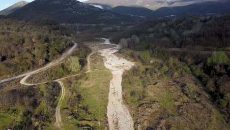 Aerial-ascend-and-top-down-view-over-dried-up-river-with-empty-riverbed-surrounded-by-mountains