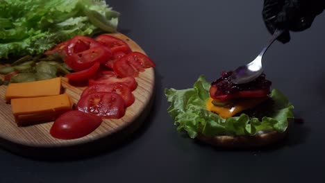 chef in black gloves adding caramelized onions on top of burger base with fresh lettuce, cheese, and tomato