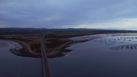 flight over the scottish ocean bridge at sunset, as the aerial view unveils a captivating scene of a long street and a picturesque brown landscape stretching beyond