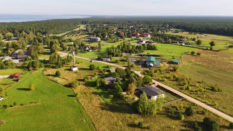 small latvian neighborhood in jurkalne during sunny day. houses and homes with farm field and main street. forest trees and baltic sea in background.