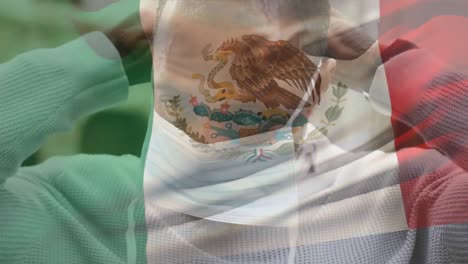 Animation-of-flag-of-mexico-waving-over-man-wearing-face-mask-during-covid-19-pandemic