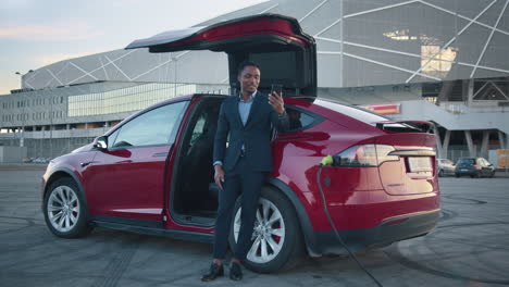hombre de negocios usando un teléfono al lado de un coche eléctrico rojo