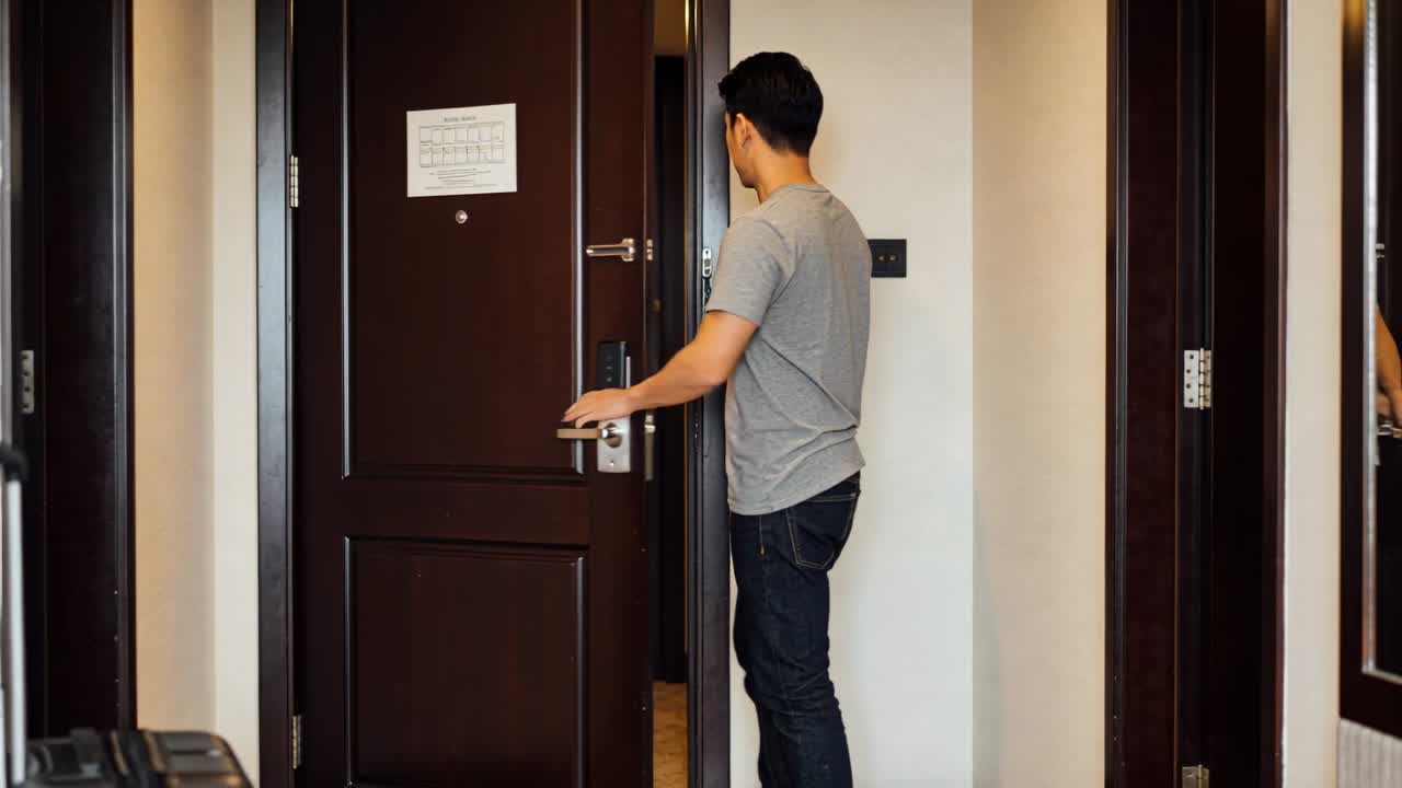 Male traveler tapping keycard on lock, opening hotel door and entering on arrival with suitcase