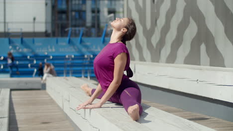 woman performing yoga splits outdoors on a park bench