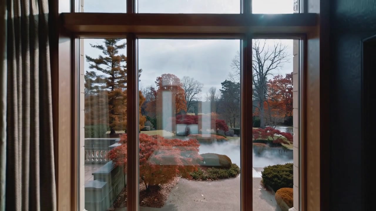 Sliding camera revealing wood-framed window, raindrops, reflection holding phone, showing garden