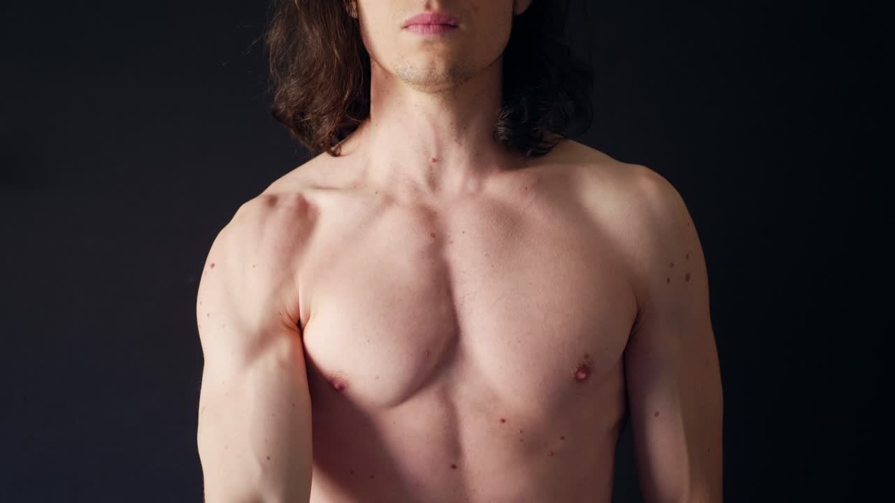 un fuerte hombre blanco sin camisa entrenando los músculos de sus hombros con un entrenamiento de banda de resistencia en el gimnasio a cámara lenta