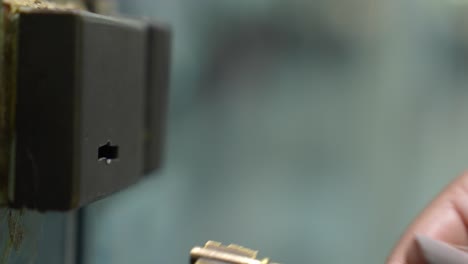 primer plano de la mano de una mujer caucásica sosteniendo una llave e insertándola en una cerradura para abrir una puerta de vidrio de una tienda