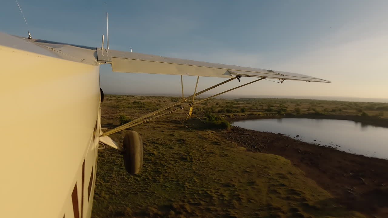 Kleines Flugzeug in Seitenansicht über grasbewachsenen Büschen und einem Gewässer